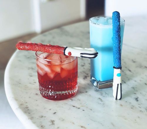 Two colorful drinks on a marble surface, each topped with a decorative candy stick resembling a lightsaber.