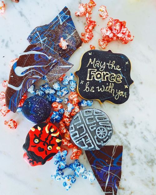 Colorful Star Wars-themed cookies and popcorn scattered on a surface, with a sign reading "May the Force be with you."