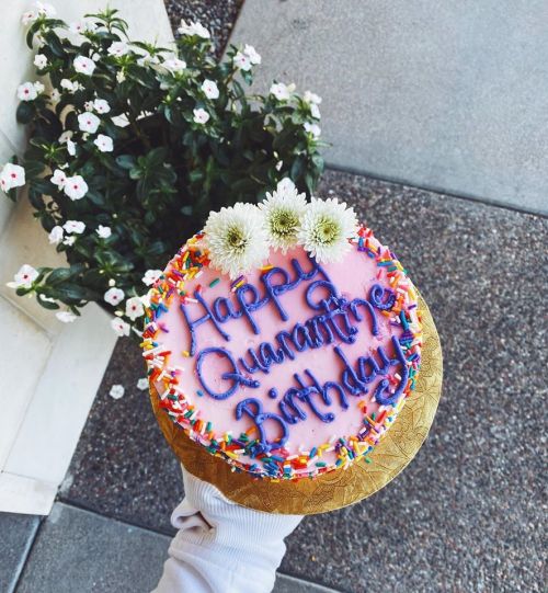 A colorful birthday cake with "Happy Quarantine Birthday" written in purple icing, topped with flowers and sprinkles.