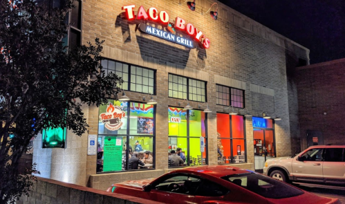 Exterior of Taco Boys Mexican Grill at night, featuring colorful windows and a red car parked outside.