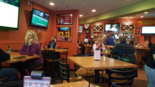 A lively restaurant scene with patrons at tables, watching sports on TVs, and enjoying food and drinks.