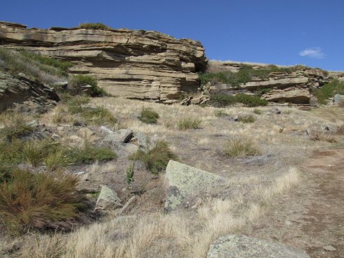 Rocky landscape with layered cliffs, sparse vegetation, and a clear blue sky.
