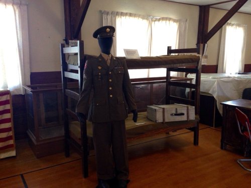 A military uniform displayed on a mannequin next to a bunk bed in a museum setting.