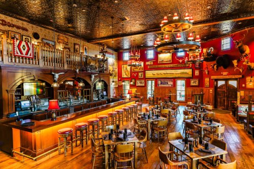 A rustic restaurant interior featuring a long bar, wooden tables, and decorative taxidermy on the walls.