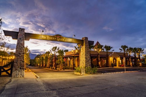 Entrance to The Ranch at Death Valley, featuring stone archway and palm trees under a dramatic evening sky.