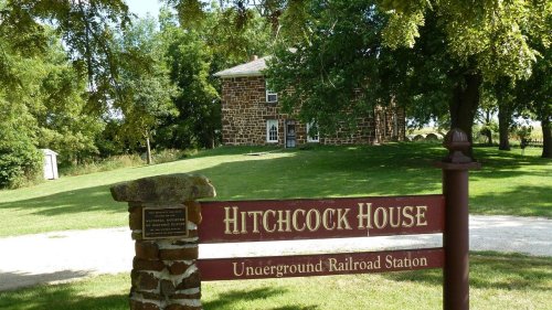 Sign for Hitchcock House, an Underground Railroad station, with a historic stone building in a green landscape.
