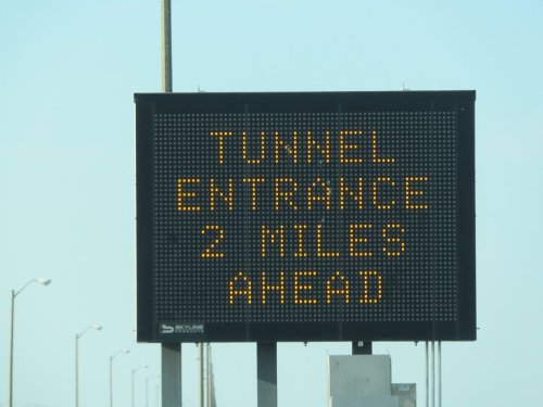 Digital sign indicating "Tunnel Entrance 2 Miles Ahead" on a clear day.