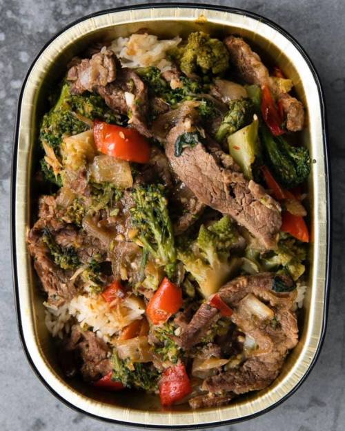 A tray of stir-fried beef with broccoli, bell peppers, and onions served over rice.