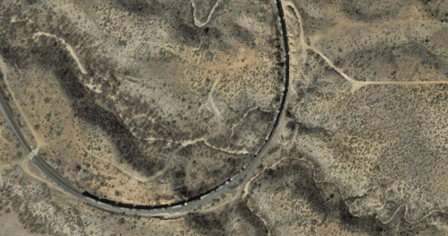 Aerial view of a winding road through arid, mountainous terrain with sparse vegetation.