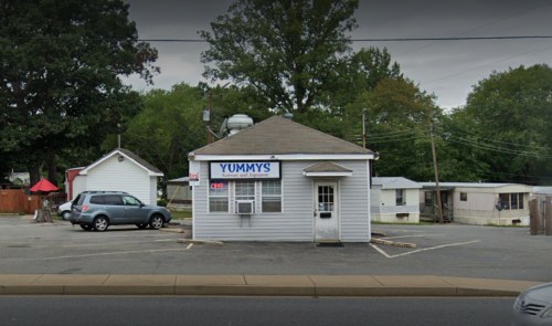 A small restaurant named "Yummy's" with a gray exterior and a sign indicating it's open, surrounded by parking and mobile homes.