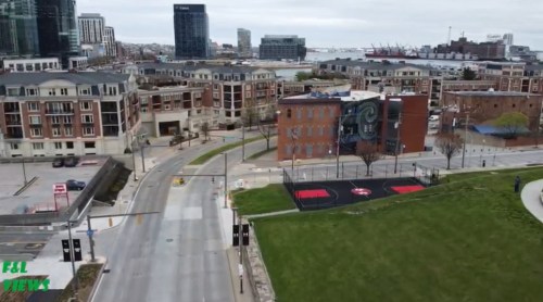 Aerial view of a cityscape featuring buildings, a park, and basketball courts near a waterfront.
