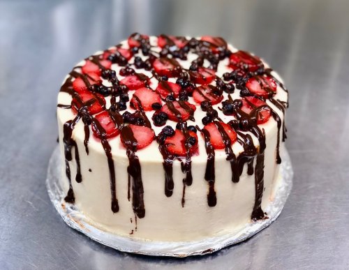 A round cake topped with strawberries and chocolate drizzle, sitting on a silver surface.