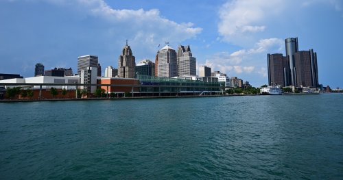 City skyline with modern buildings along a waterfront under a partly cloudy sky.