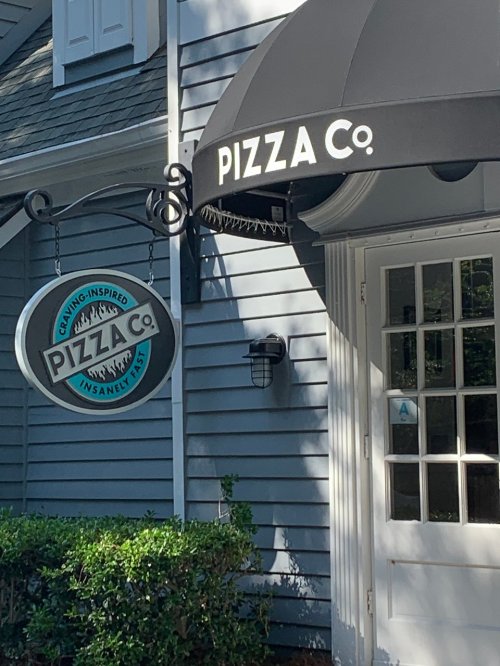 A storefront with a black awning displaying "PIZZA Co." and a sign that reads "Pizza Co. - Insanely Tasty."