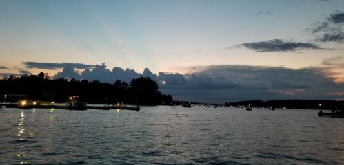 A serene lake at dusk, with boats on the water and a colorful sky filled with clouds and fading light.