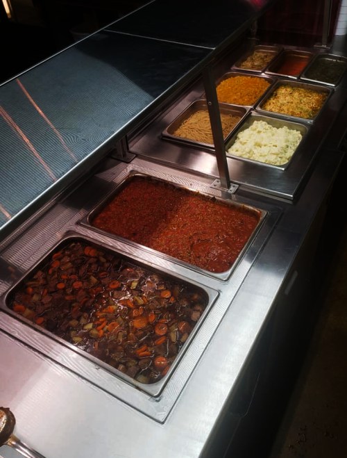 A buffet display with various trays of food, including stews, pasta, and side dishes.