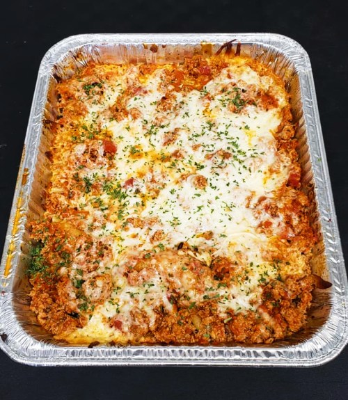 A silver tray filled with baked pasta topped with melted cheese and herbs, golden and bubbly.