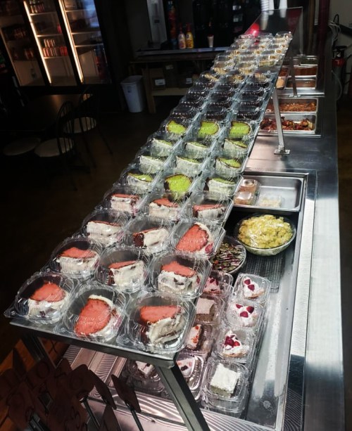 A display of assorted desserts in clear containers arranged on a metal counter in a café setting.