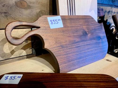 A wooden cutting board with a handle, priced at $55, displayed on a rustic wooden surface.