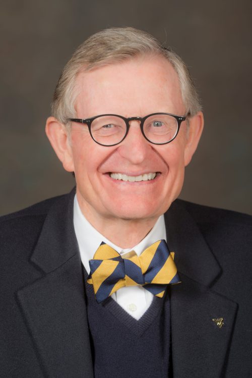 A smiling man with glasses and a bow tie, wearing a dark blazer and white shirt, against a neutral background.