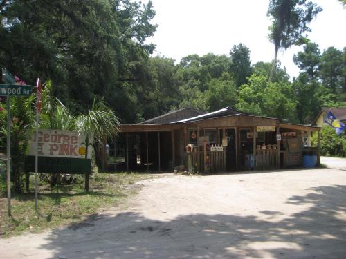 A rustic roadside market with a wooden structure, signs for fresh vegetables, and surrounded by greenery.