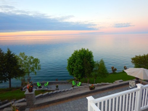 Serene lakeside view at sunset, featuring calm waters, lush greenery, and a stone pathway leading down to the shore.