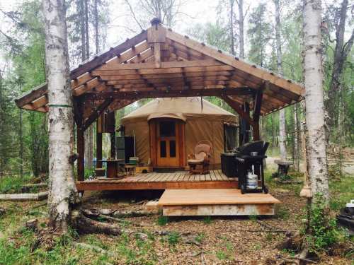 A cozy yurt with a wooden deck, surrounded by trees in a serene forest setting.