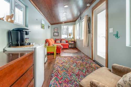 Cozy interior with a colorful rug, seating area, coffee maker, and large windows letting in natural light.