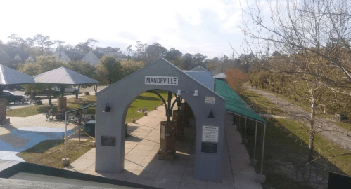 A covered pavilion with the sign "Mandeville," surrounded by trees and pathways in a park setting.