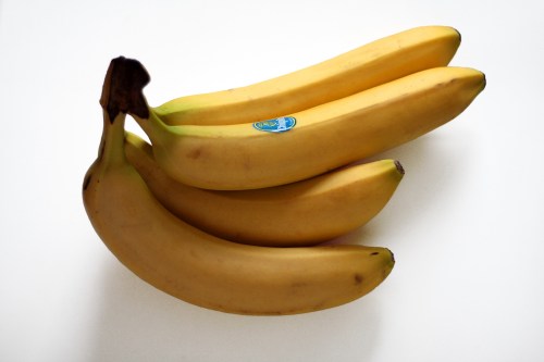Three ripe bananas with a sticker on one, resting on a white surface.