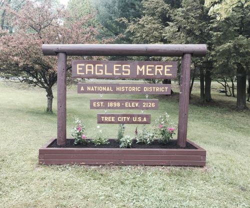 Sign for Eagles Mere, a National Historic District, established in 1898, with flowers and greenery around it.