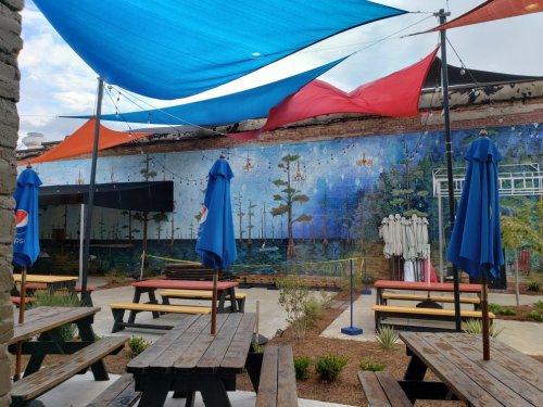 Outdoor seating area with colorful canopies, a mural of trees, and a garden setting.