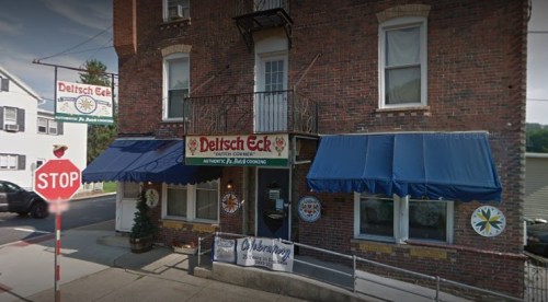 Exterior of Delitsch Eck restaurant with blue awnings, a stop sign nearby, and decorative elements on the brick facade.
