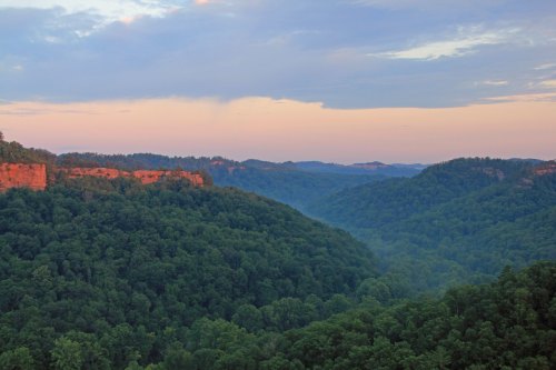 A scenic view of lush green hills and cliffs under a pastel sky at dusk.