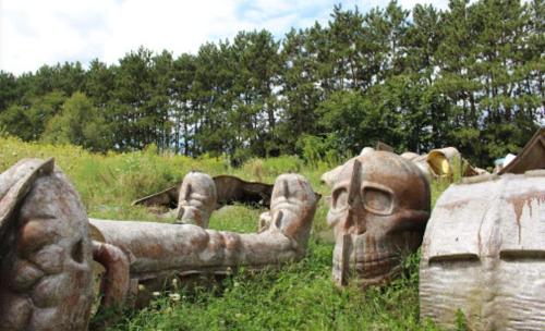 A grassy area with large, weathered skull sculptures surrounded by trees and wildflowers.