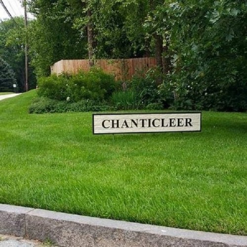 A sign reading "CHANTICLEER" on a grassy area surrounded by trees and a wooden fence.