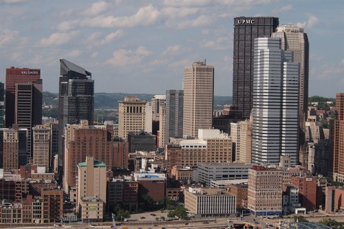 Aerial view of a city skyline featuring tall buildings and a mix of modern and historic architecture under a blue sky.