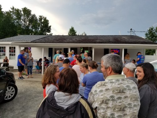 A crowd of people waiting in line outside a small restaurant on a cloudy day.
