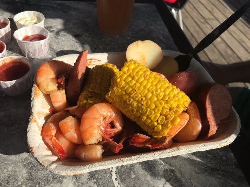 A seafood platter with shrimp, corn on the cob, sausage, and potatoes, served on a tray with dipping sauces.
