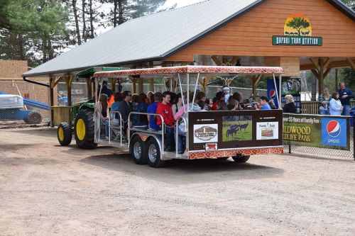 A tractor-drawn wagon filled with people arrives at a rustic building in a park setting.