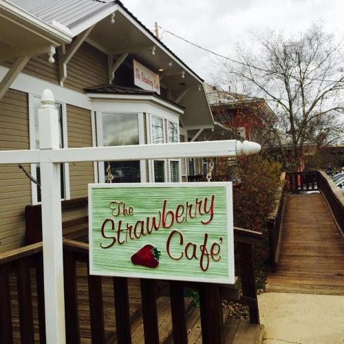 Sign for "The Strawberry Café" outside a charming café with a wooden deck and cloudy sky in the background.