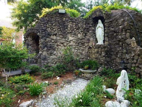 A serene garden featuring stone walls, statues, and lush greenery, creating a peaceful, natural atmosphere.