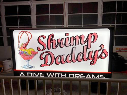 Neon sign for "Shrimp Daddy's" featuring a shrimp cocktail and the tagline "A Dive with Dreams."