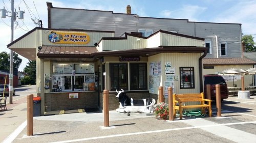 A small popcorn shop with a sign for "20 Flavors of Popcorn," featuring outdoor seating and a cow statue.