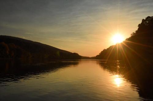Sunset over a calm river, with mountains in the background and reflections shimmering on the water's surface.