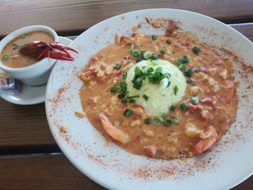 A plate of shrimp and grits topped with green onions, alongside a cup of crawfish bisque.