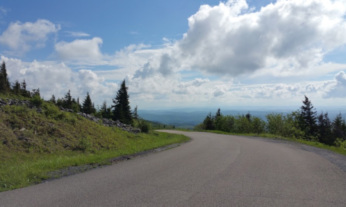 A winding road through green hills under a blue sky with fluffy clouds and distant mountains.