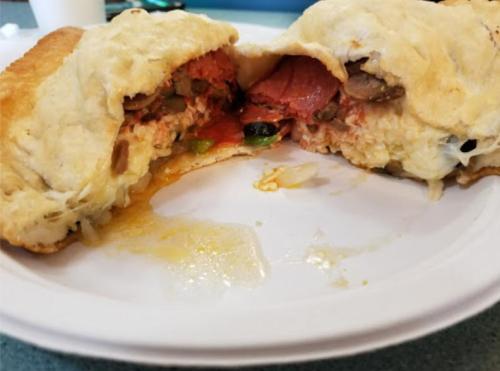 A partially eaten calzone filled with cheese, pepperoni, mushrooms, and vegetables on a white plate.