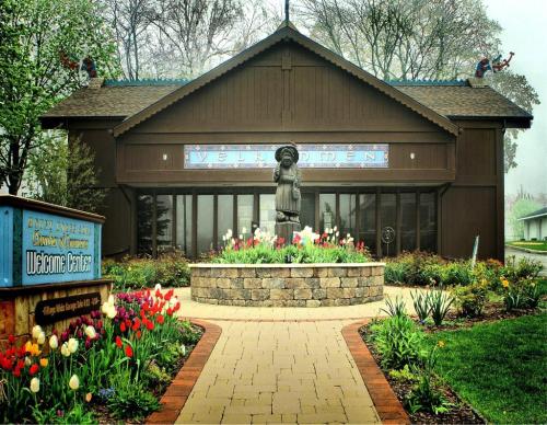 A welcoming center with a statue in front, surrounded by colorful tulips and greenery, under a cloudy sky.