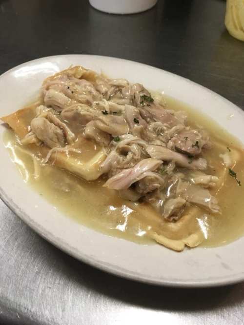 A plate of chicken and noodles in a savory broth, garnished with herbs.